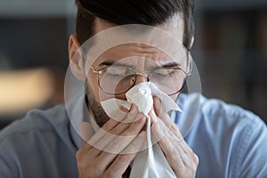 Man holding tissue sneezing blowing runny nose feels unhealthy closeup