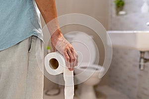 Man holding toilet paper roll in bathroom. Man suffers from diarrhea. Diarrhea concept