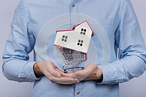 Man holding toy shopping cart and model home. Buying house on credit concept