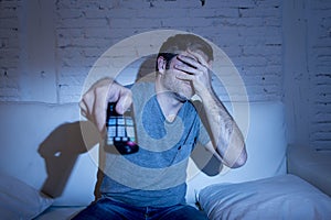 Man holding tv remote control sitting at living room couch watching television blocking his eyes