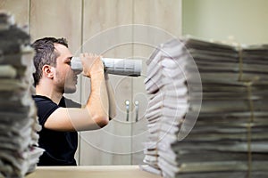 Man holding two twisted roll newspaper. Metaphor or allegory with binoculars. Selective focus on the face