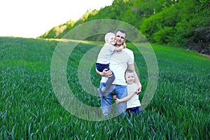 A man holding two young boys in a field of vibrant green grass.