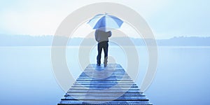 Man Holding an Umbrella on a Jetty by Tranquil Lake Concept