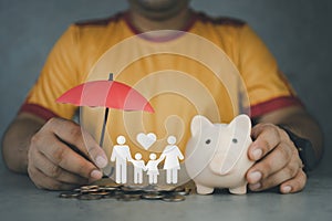 Man holding umbrella with a piggy bank and paper family. Insurance concept