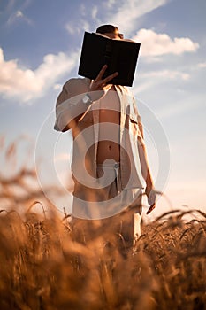 man holding up Bible in a wheat field