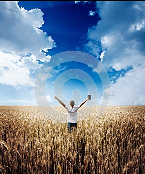 Man holding up Bible in a wheat field