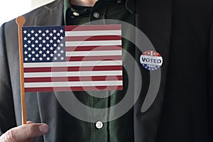Man holding USA flag with I Voted Today sticker one coat lapel