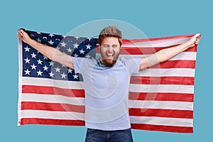 Man holding USA flag and looking at camera with rejoicing look, celebrating national holiday.