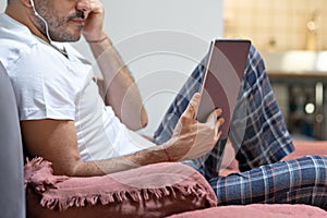 Man holding using digital tablet and headphones in bed at home with pijama. Online education, working, video call