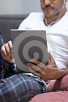 Man holding using digital tablet and headphones in bed at home with pijama. Online education, working, video call