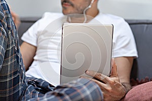Man holding using digital tablet and headphones in bed at home with pijama. Online education, working, video call