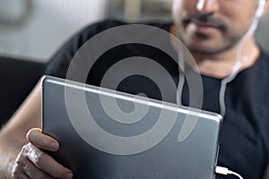 Man holding using digital tablet and headphones sitting on a sofa. Online education, working, video call