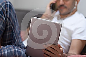 Man holding using digital tablet, smartphone and headphones in bed at home. Online education, working, video call