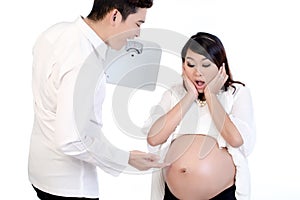 Man holding weigh scale pointing finger at his pregnant wife`s belly