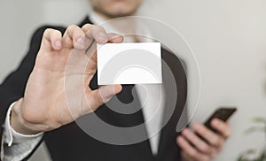 Man holding white business card,Man wearing white shirt and showing blank white business card. Blurred background. Horizontal mock
