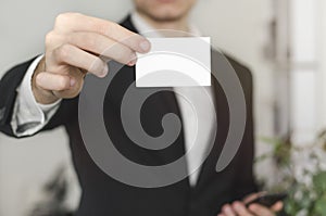 Man holding white business card,Man wearing white shirt and showing blank white business card. Blurred background. Horizontal mock