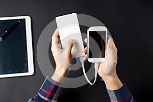 Man holding a white cellphone connected to a power bank