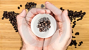 Man is holding white ceramic cup full of coffee beans