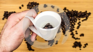 Man is holding white ceramic cup full of coffee beans