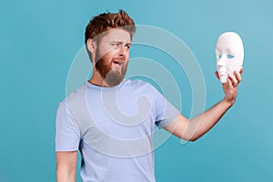 Man holding white mask in hands and looking with open mouth, despises hidden personality.