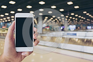 A man holding white mobile phone with blank black screen while standing and waiting for baggage claim