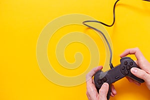 Man holding wired gamepad or video game controller on yellow background. Top view, flat lay