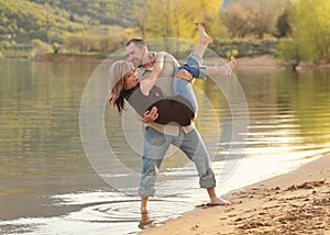 Man holding woman playfully on lake shore