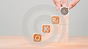 Man holding a wooden cube block with goal icon and OKR or Objectives and Key Results text.
