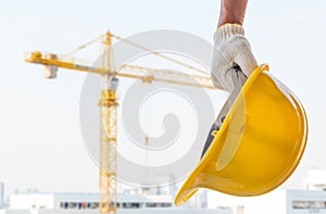 Man holding the yellow safety helmet at construction site with crane background