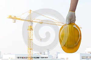 Man holding the yellow safety helmet at construction site with crane background