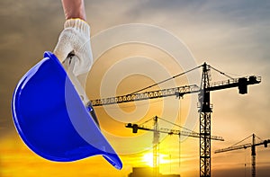 Man holding the yellow safety helmet at construction site with crane background silhouette