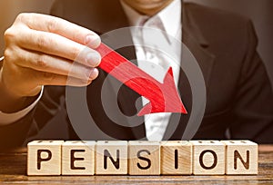 A man holds an arrow down over wooden blocks with the word Pension. Fall / reduction pension payments. Retirement. Financing