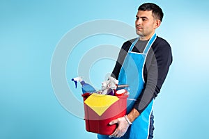 A man holds a bucket with various household cleaning products. Gender equality. Blue background, side space