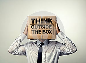 A man holds a cardboard box on his head with the text phrase words think outside the box written on it