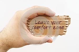 A man holds a cardboard in his hand on which it is written - Leave your comfort zone