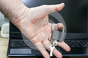 A man holds a closed padlock with keys in his hand against the background of a laptop concept data protection internet censorship