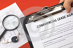 Man holds commercial lease agreement in hand. Clipboard with official document. Background with real property papers and