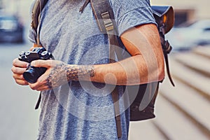 A man holds a compact film camera with tattooed arms.