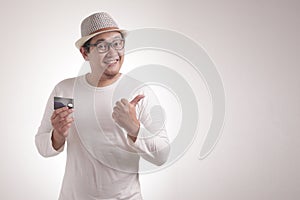 man holds credit card, smiling and pointing to the side, copy space