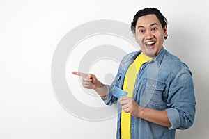 Man holds credit card, smiling and pointing to the side, copy space