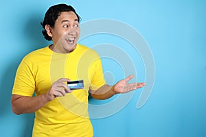 Man holds credit card, smiling and pointing to the side, copy space