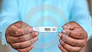 Man holds digital thermometer with temperature reading in Fahrenheit closeup