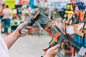 A man holds a drill for drilling in his hands. Concept man selects a product in a hardware store