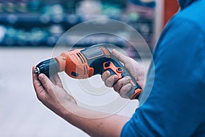 A man holds an electric drill in his hand for drilling. A buyer in a hardware store selects a product