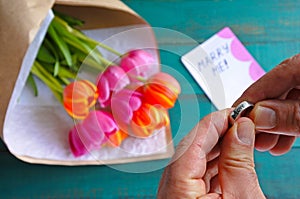 Man holds an engagement ring over a Marry me message note