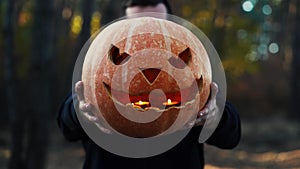 Man holds a festive pumpkin in front of him in the woods