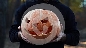 man holds a festive pumpkin in front of him in the woods