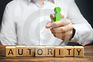 A man holds figures of people in a fist and the word Authority. High status and respect, reputation and importance. Business