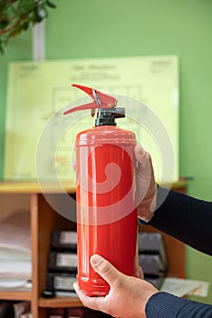 man holds a fire extinguisher in his hands against the background of a fire evacuation plan.