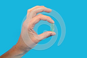 A man holds a fish oil capsule with his fingers on a blue background. Free space for text